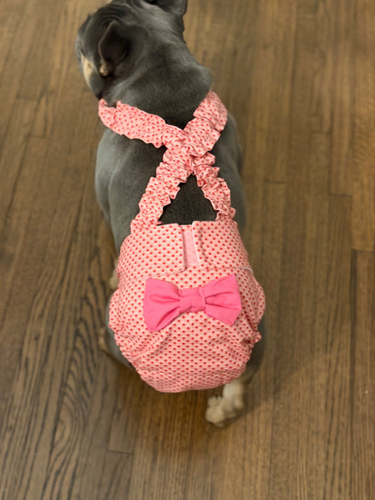 Dog wearing a coral pink diaper with a bow on a wooden floor